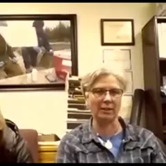 Two people sitting in an office with a bookcase and desk behind them.