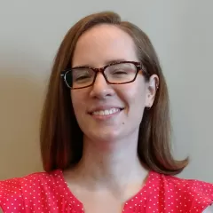 A smiling, light-skinned woman with glasses and shoulder-length brown hair