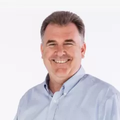 A man in a blue shirt smiles in front of a white backdrop