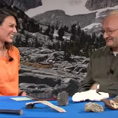 Maggy Benson and Dr. Hans Sues are sitting at a table with a variety of rocks and tools in front of them.