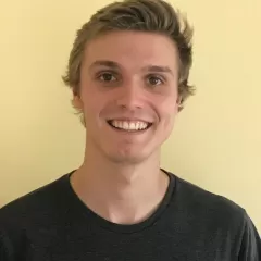 Light-skinned man smiles in front of a pale yellow wall