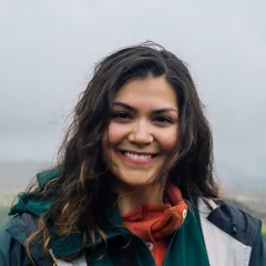 A smiling woman with medium-light skin tone and dark wavy hair