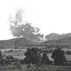 A cloud of volcanic ash rising out of small hills and over fields