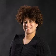 A headshot of an African American woman looking at the camera with a dark background. 