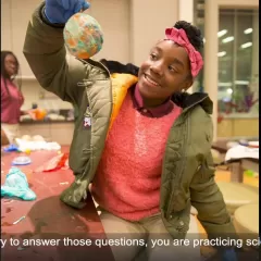 A girl holding a craft ball she made during a science program at the museum.