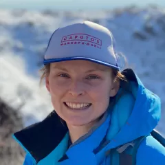 A woman in a baseball cap and blue jacket smiles at the camera