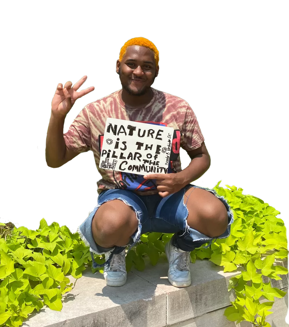 African American man with orange hair holding a peace sign with fingers and a sign that says nature is the pillar of the community