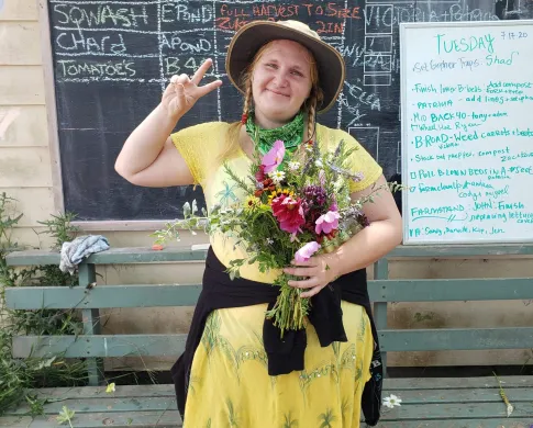 woman in yellow dress and brown hat holding wild flowers 