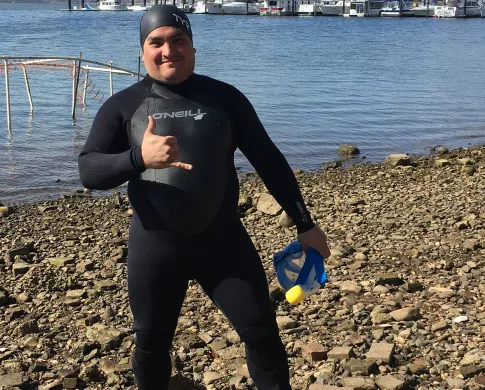 a man in a black wetsuit standing on the bank of a river 