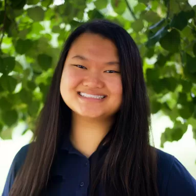 A smiling woman standing in front of a tree