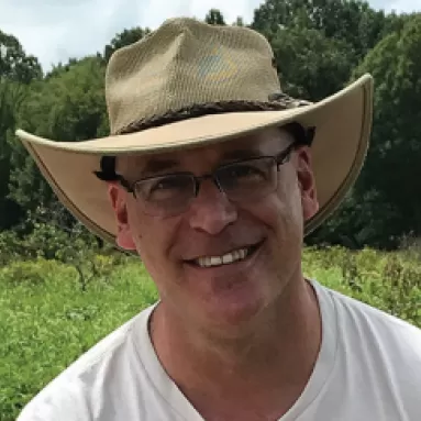 A man wearing a hat and glasses standing in a grassy field