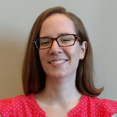 A smiling, light-skinned woman with glasses and shoulder-length brown hair