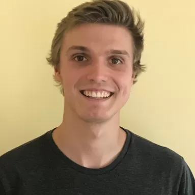 Light-skinned man smiles in front of a pale yellow wall