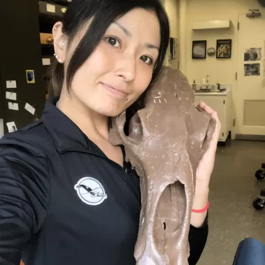 image of Japanese woman in a black lab coat holding long fossil skull