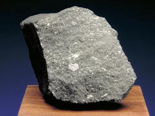 Allende Meteorite - a rock with sharp edges displayed on a wood surface