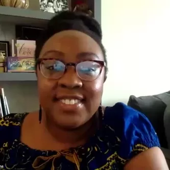 A medium-dark skinned woman smiling in front of a bookcase