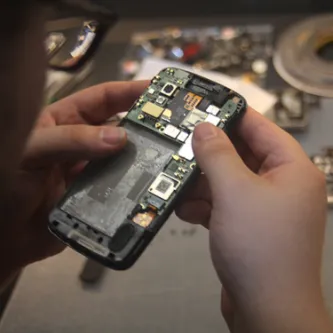 Two hands holding a cellphone that has its back removed, exposing the circuitry and parts.