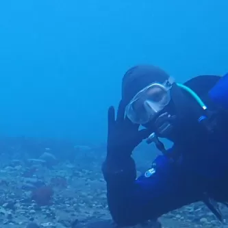 A scuba diver rests his elbow and leg on the sea floor next to a data logger tethered to a weight on the bottom.