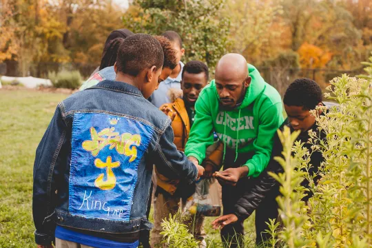 man in green sweatshirt looking at garden with younger men