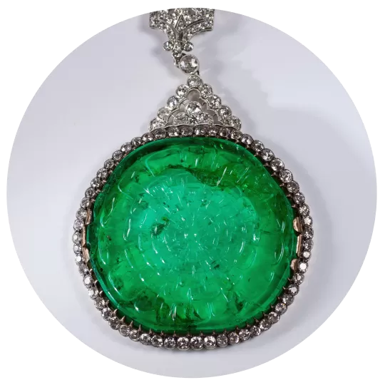 A round green gem surrounded by diamonds on a necklace. 