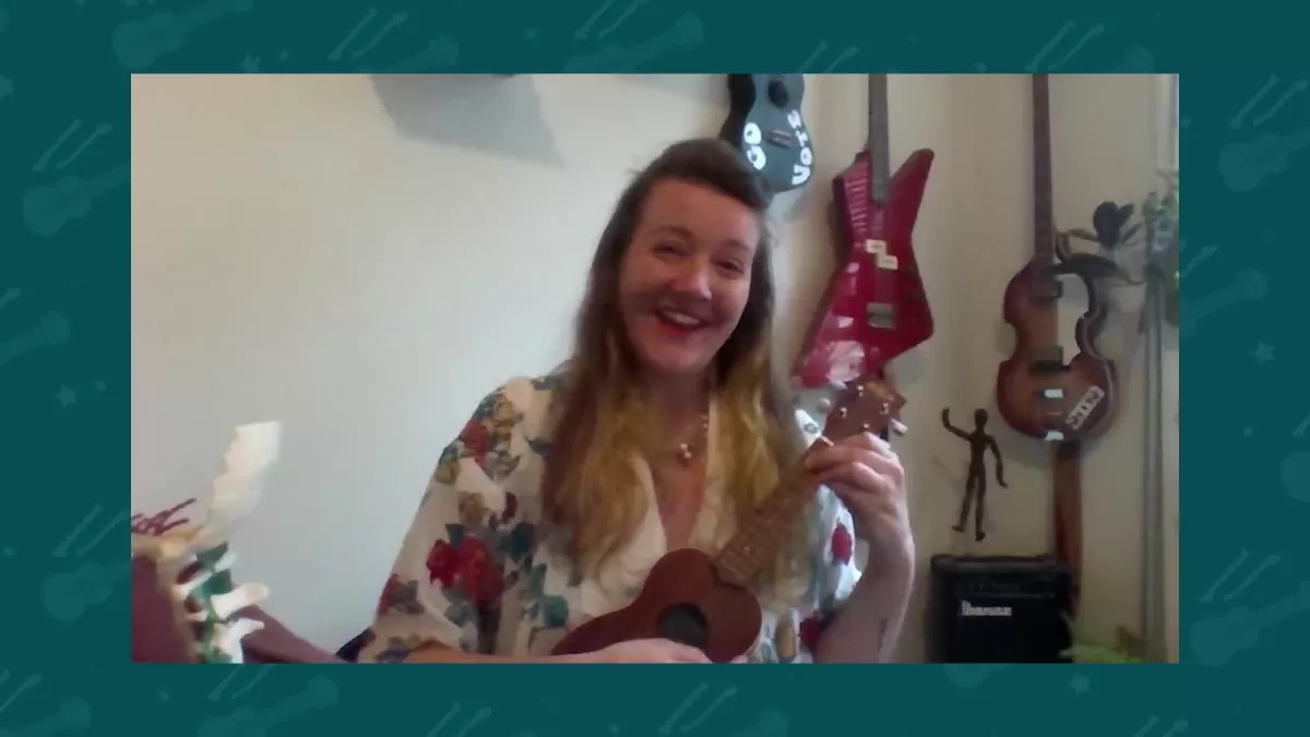 A woman smiling and playing a ukulele.