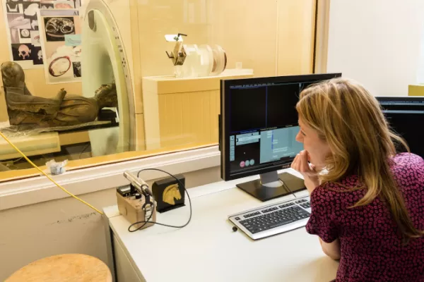 Scientist at computer, watching sculpture go into CT scanner