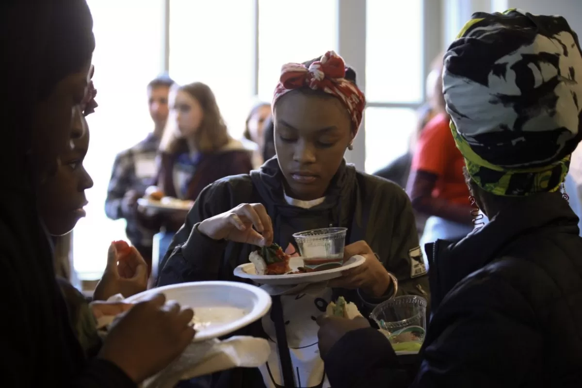 A teenage girl holding a paper plate and picking up a piece of food from it.